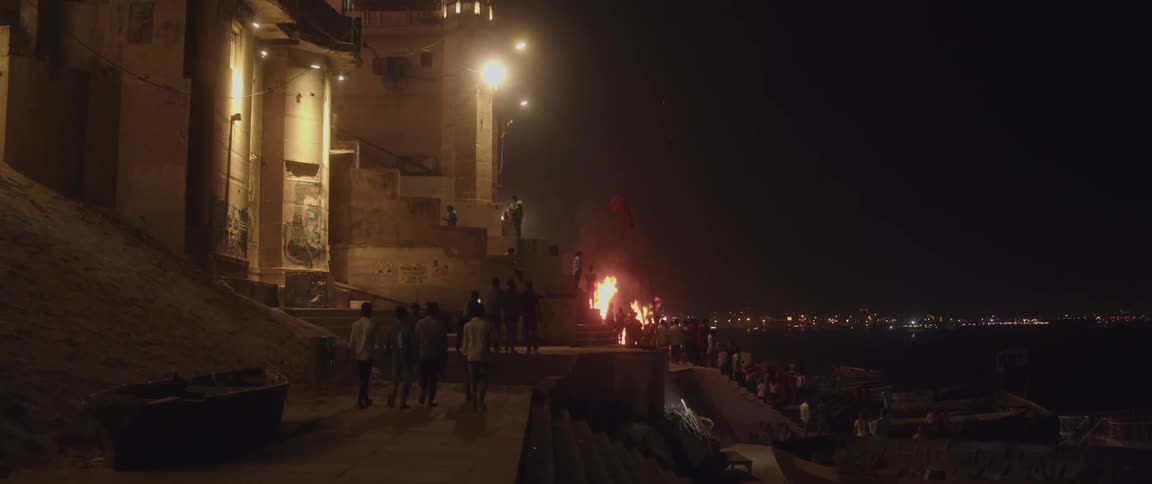 A group of people gathers around bonfires on the steps of a temple