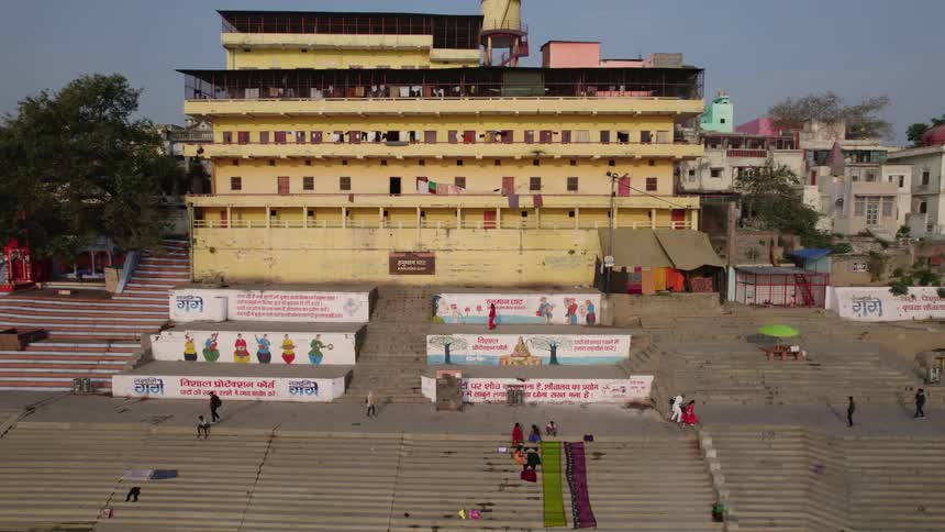 People are walking on sidewalks and sitting on steps with colorful murals near buildings with balconies and porches