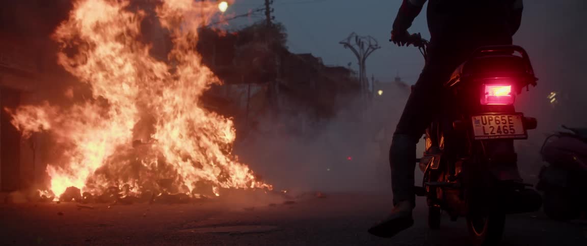 Motorcycles drive past a burning pile downtown