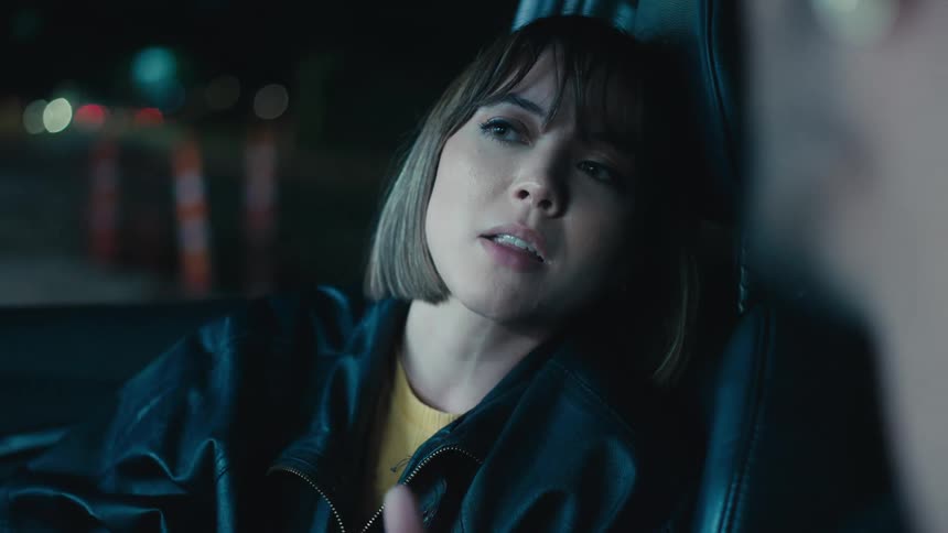 Woman with bob haircut and black leather jacket talks to man in car