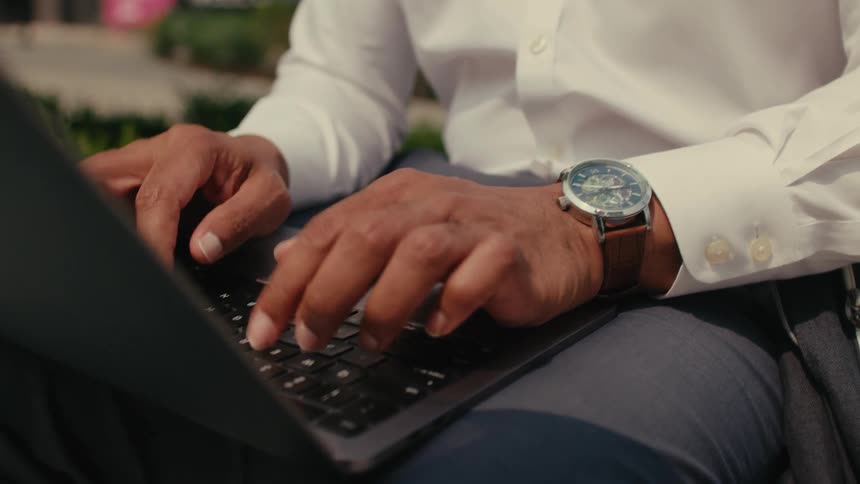 Man sits near plants and types on laptop in his lap