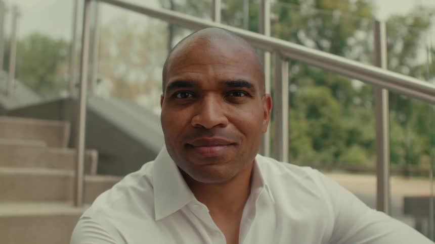 Man in white shirt smiles at camera sitting on stairs