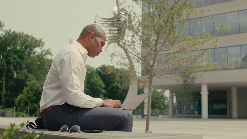 A man is sitting outdoors and typing on laptop