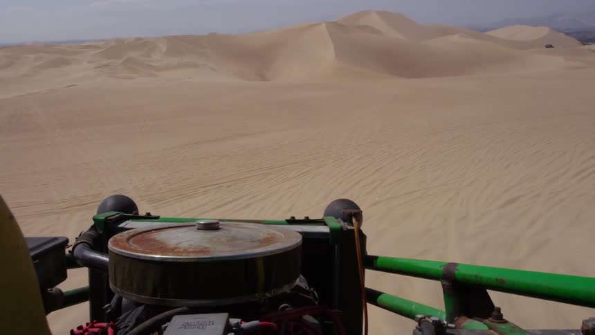 A vehicle is driving over sand dunes