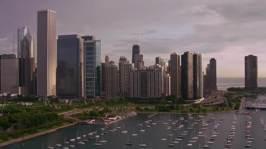 Aerial view of boats floating on water next to city skyline at dusk