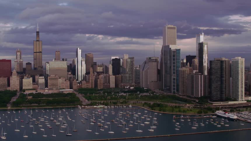 Towers and skyscrapers overlook boats sailing in the water near the metropolitan city on the coast under a cloudy sky