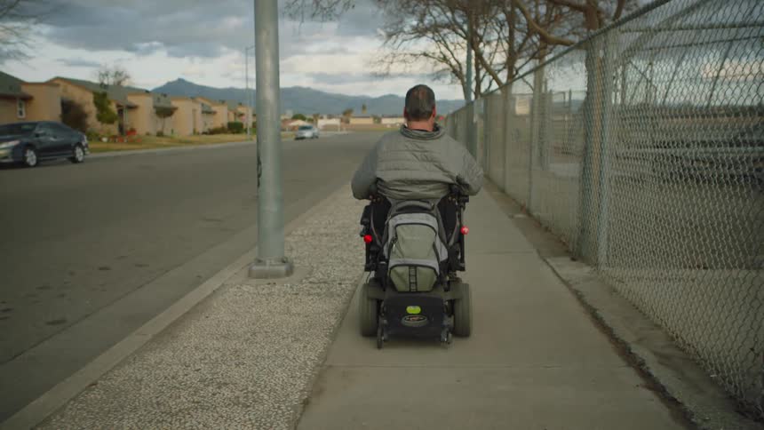 A man drives a disabled motorcycle on a sidewalk