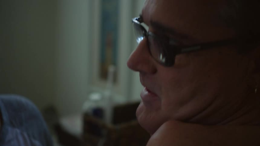 A man is lying in bed as his wife is rubbing her hands on his cheeks with a concerned look on her face