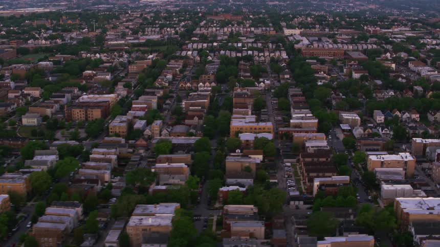Traffic moves on neighborhood streets as cars are parked in driveways and parking lots and houses are close together