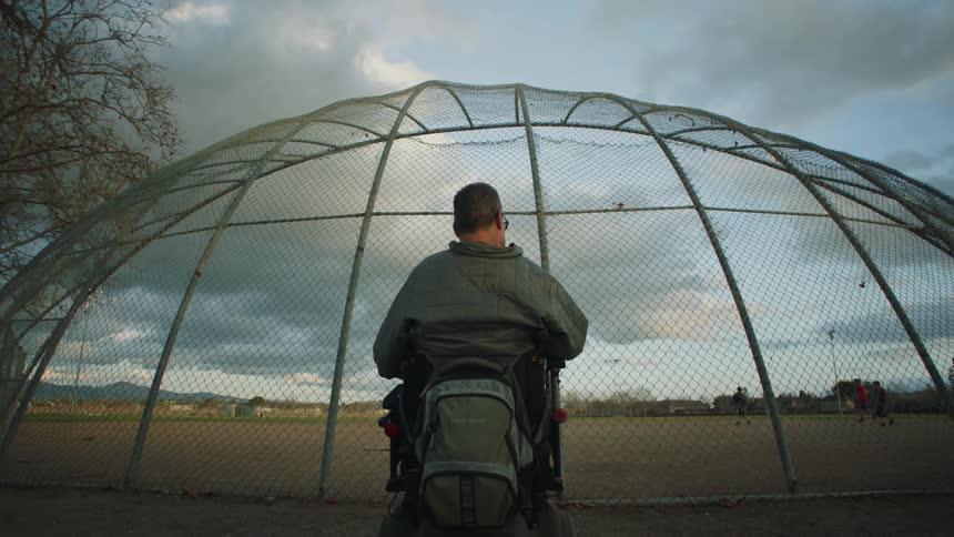 Disabled man in wheelchair watches people playing football