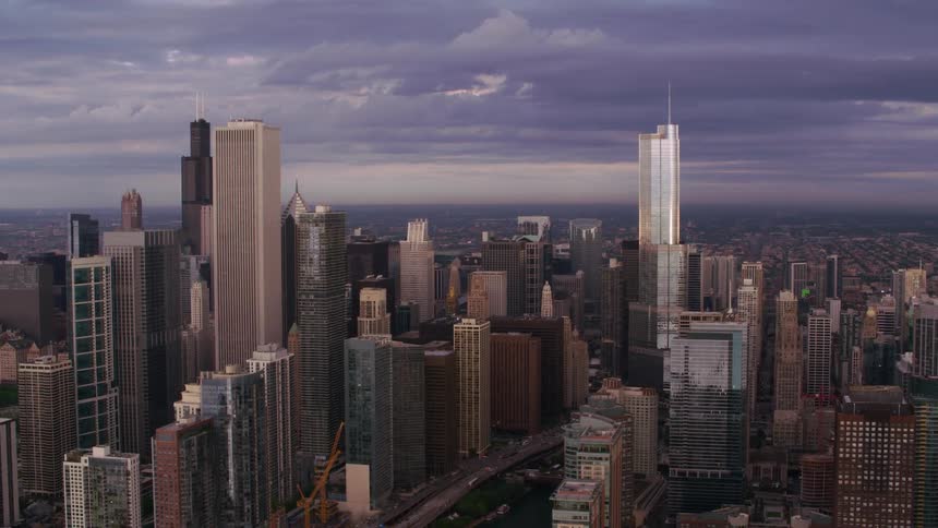 Skyscrapers along a waterway loom over a metropolis in the evening