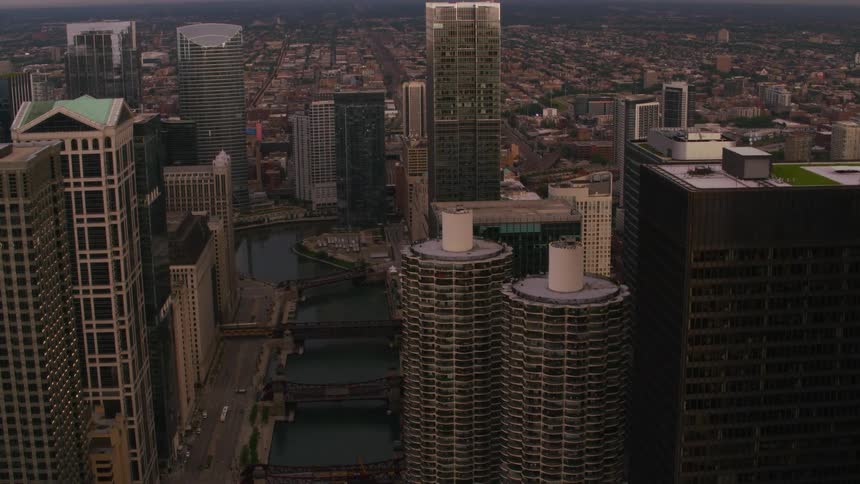 Towers and skyscrapers stand tall in a metropolitan city as traffic moves across bridges over the river and suburban neighborhoods are in the distance