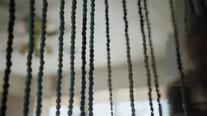 A woman walks through a door curtain made of beads