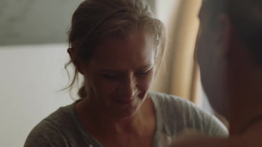 A woman laughs in a kind way as she helps a man put on a sweater
