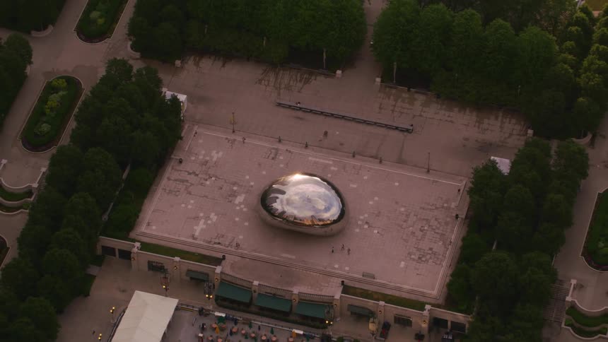 People move around large oval metal sculpture on roof of building near covered park