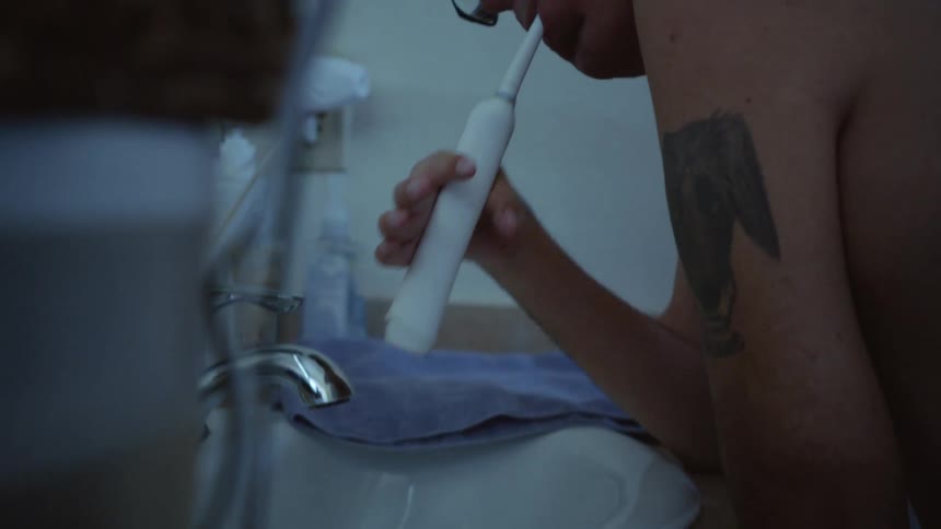 Man with disabled arms leans over sink and brushes his teeth with an electric toothbrush