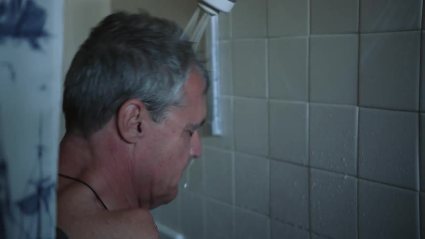 An older man is taking a shower inside of his bathroom