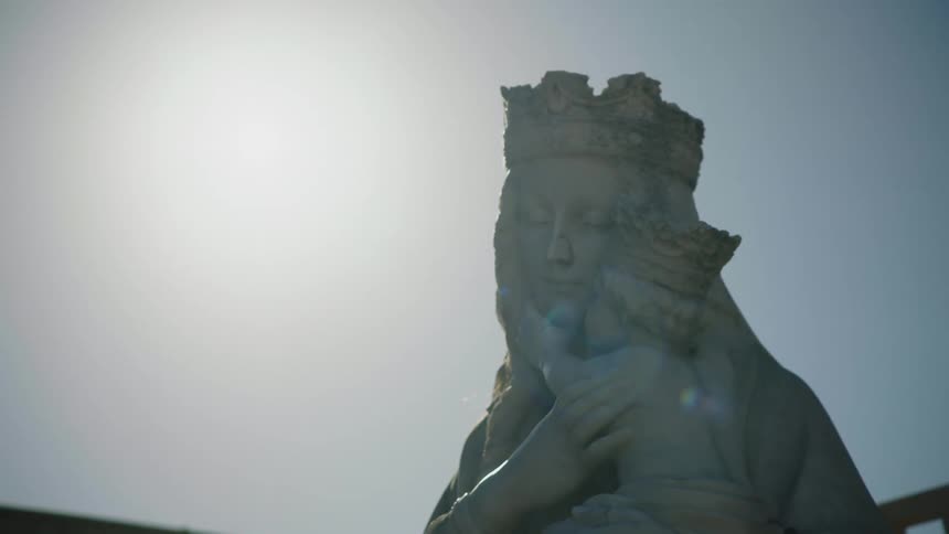 Statue of crowned virgin mary holding jesus sits under sunny sky