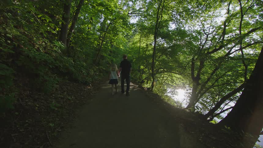 Girl walks hand in hand with grandfather using a guide cane as they travel down path near water