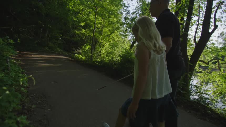 A young girl leads her blind grandfather down a path walking hand in hand