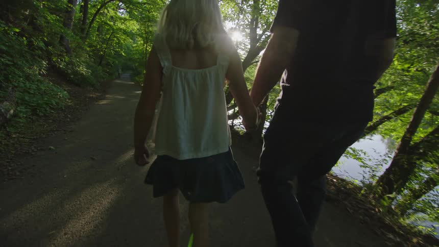 A little blond girl holders her blind grandfathers hand to guide him down a wooded trail