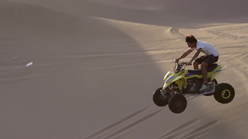 A young man jumps over a sand dune while driving a four-wheel buggy