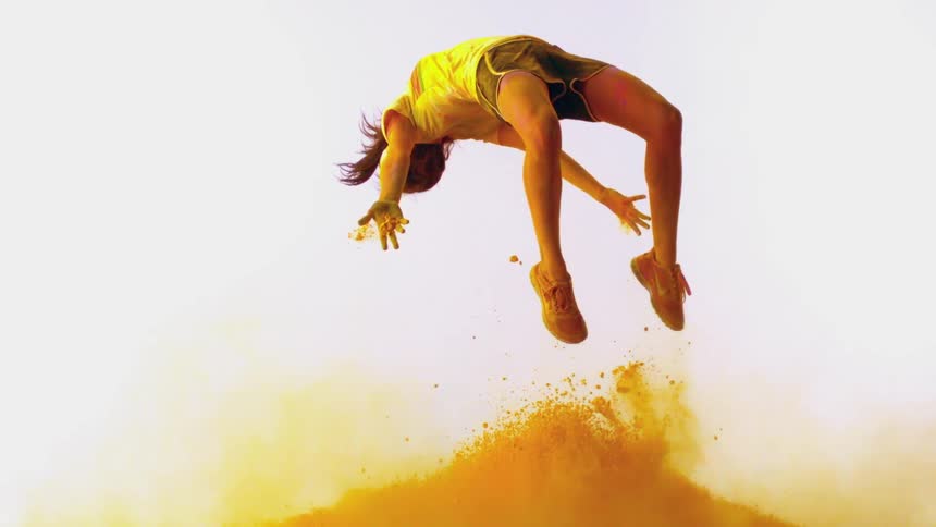 A young woman does a backflip through yellow powder