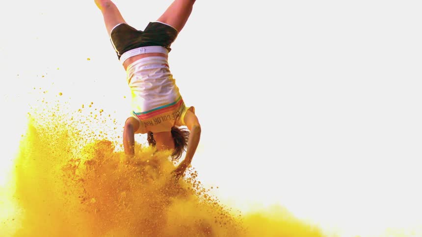A young woman flips through the air with yellow powder exploding