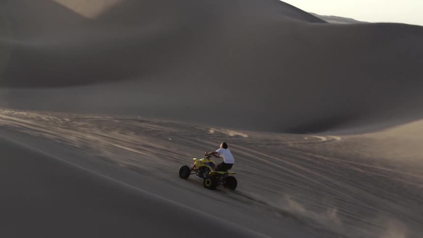 A man drives on sand dunes on a four wheeler