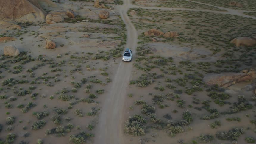 An aerial of a car driving on a dirt road in the desert