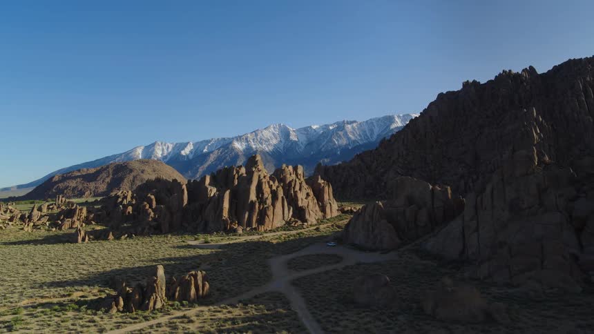 Car sits parked at base of craggy outcroppings near dirt road passing through mountains