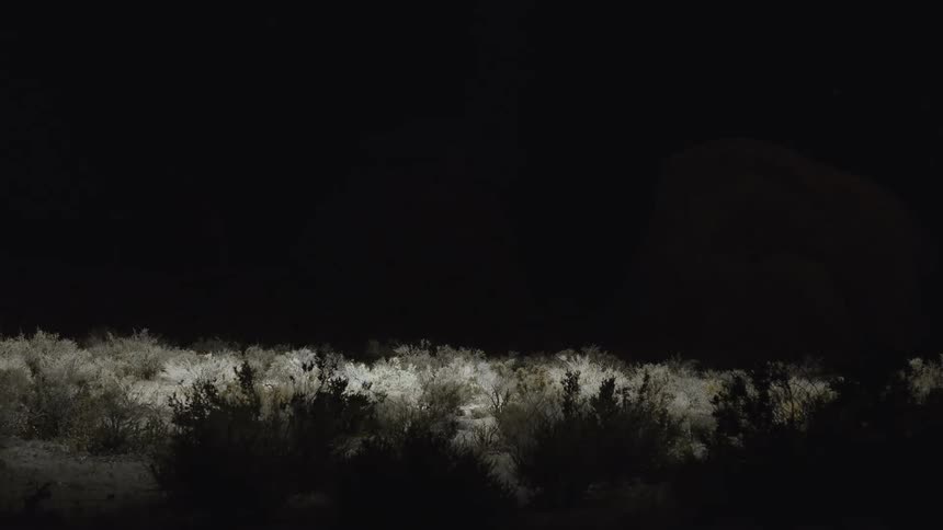 Light pans over what looks like a broken statue in a desert in the darkness search light helicopter drone light