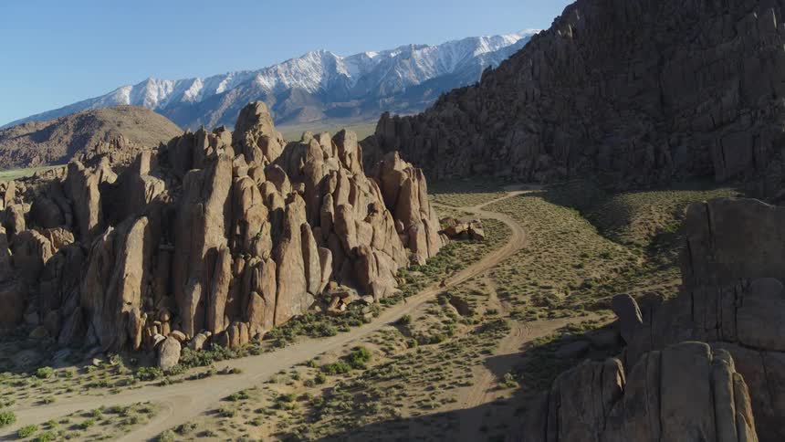 A white automobile is parked on a dirt road near rock formations and mountains under a clear sky