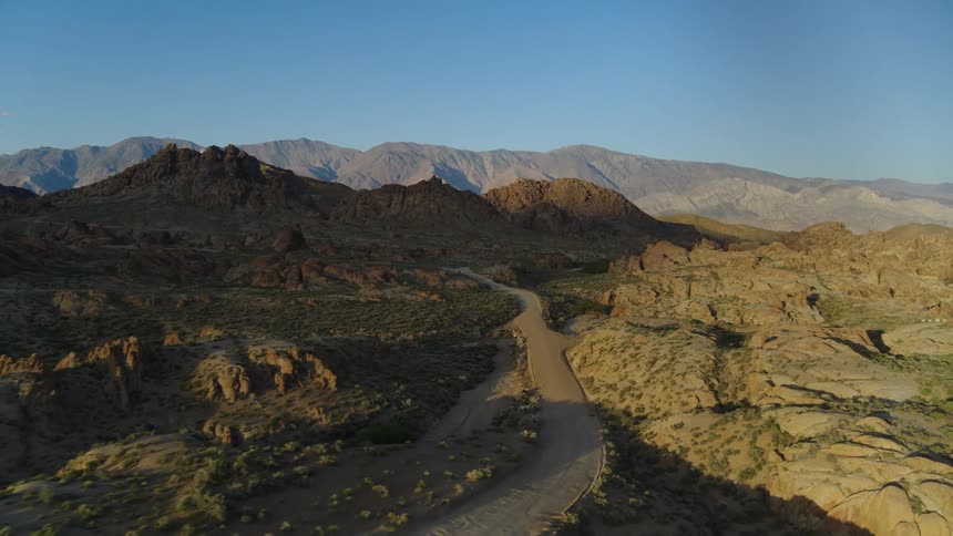 The sun shines upon a road in the desert with mountains in the distance under a clear sky
