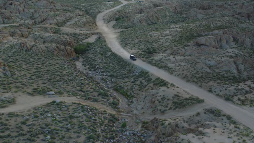 Truck kicks up dust while driving along dirt road through scrubland