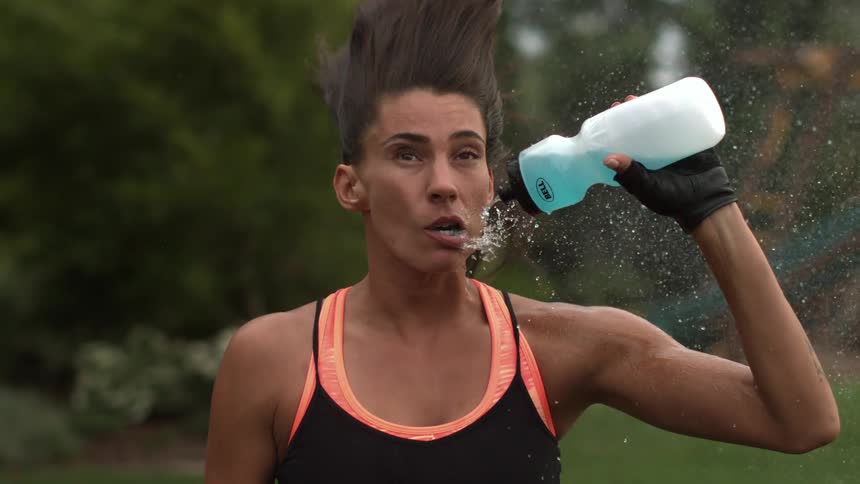 A woman tries to drink from a water bottle, but wind is blowing her face and water everywhere