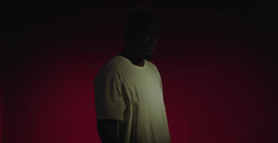 Light shines on a man as he stands in the darkness with red light behind him