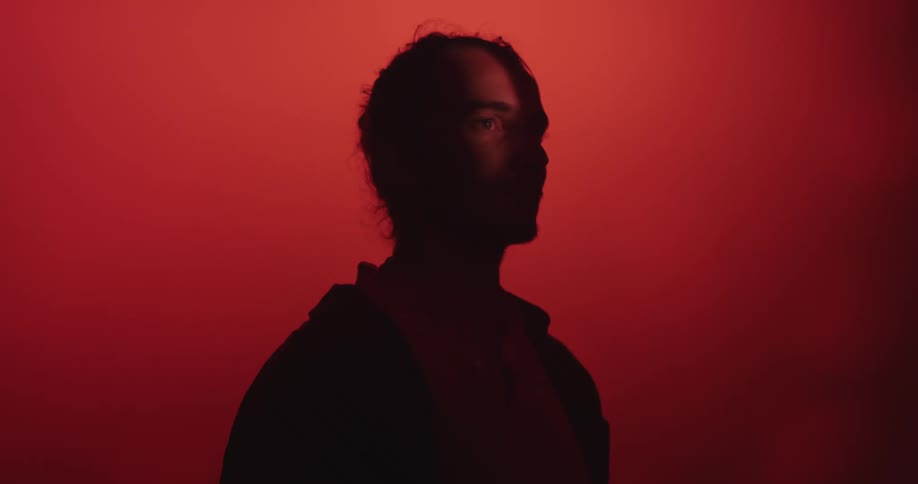 A man in silhouette in front of a red background until his eye comes into the light