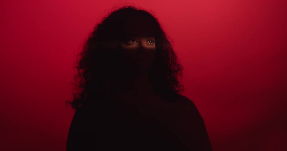 A girl in shadows turns to the camera where only her eyes become illuminated