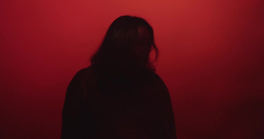A woman in silhouette against a red background until a ray of light exposes her eyes