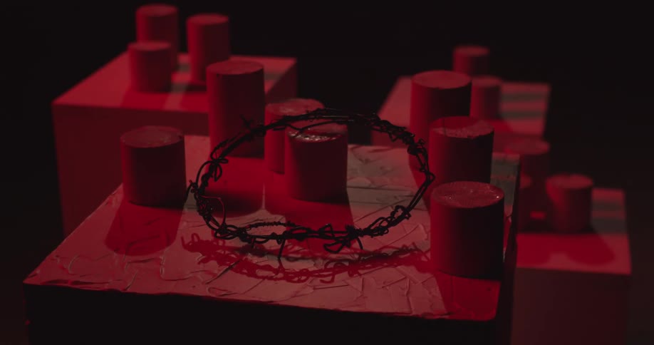 Orbiting a wood and plaster sculpture with round pegs of varying height and a crown of barbed wire sitting on top dim light with red filter