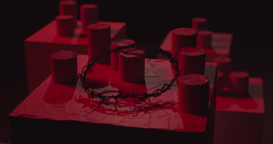 A circle of black barbed wire on top of several red cylinders and a big red cube