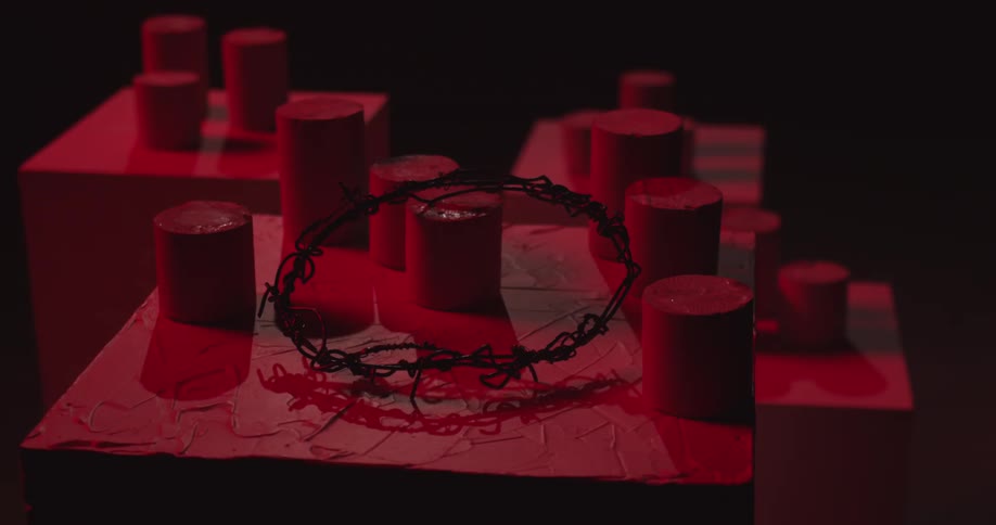 Crown of thorns sits among cylinders on pedestal in dark room
