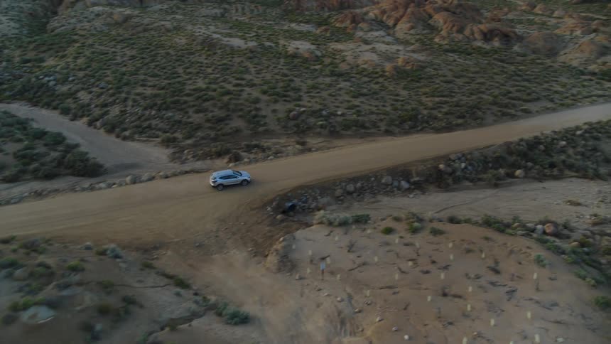 The view is of the desert area and a car is driving down the road
