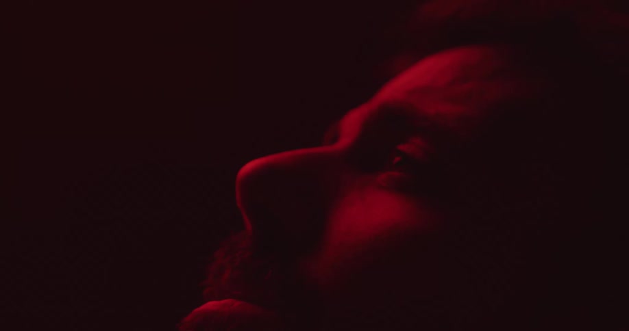 Close up of the face of a man inside a room dimly lit under red lights