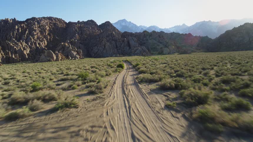 The sun shines brightly upon dirt roads running between rock formations and mountains