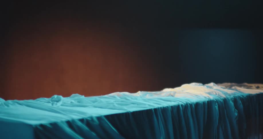 A white sheet bathed in blue light covering a wood board in front of a red wall