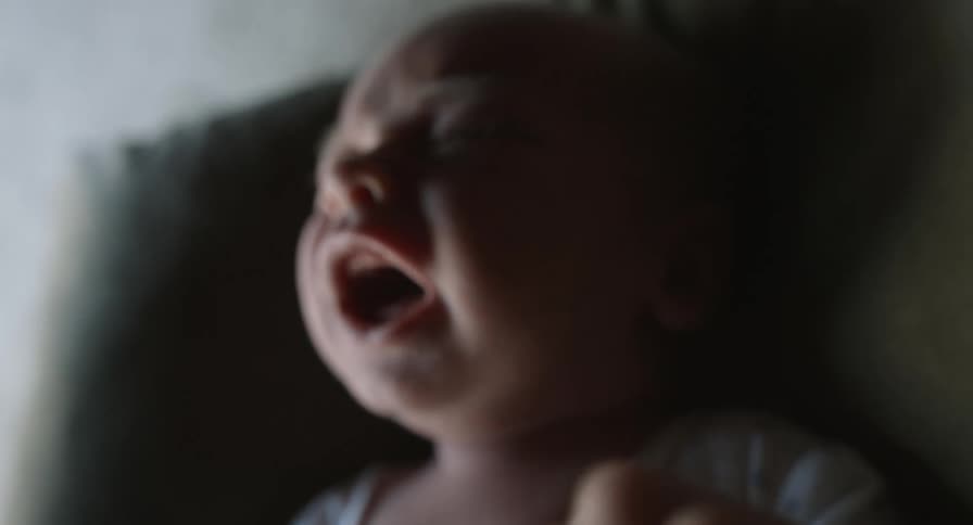 A baby is screaming and crying with their mouth wide open as their arms and legs are moving