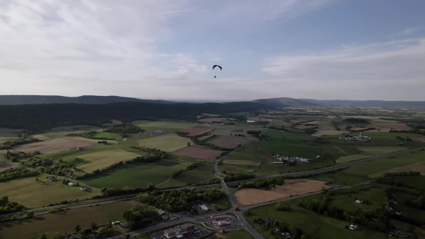 Paraglider travels over rural landscape on cloudy day