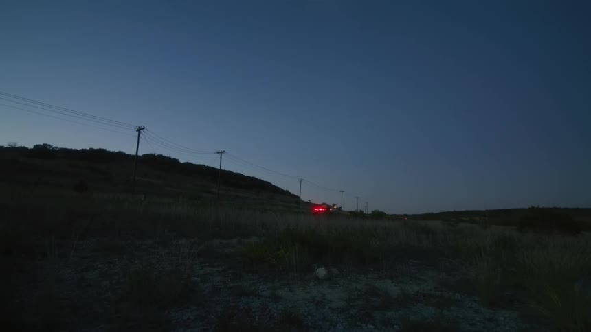 Vehicle drives on a rural road next to power lines at morning